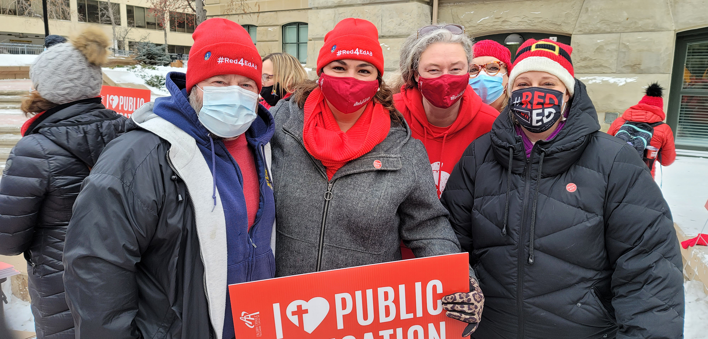 Teachers wearing masks stand together with I love public education sign outside of Alberta legislature. 