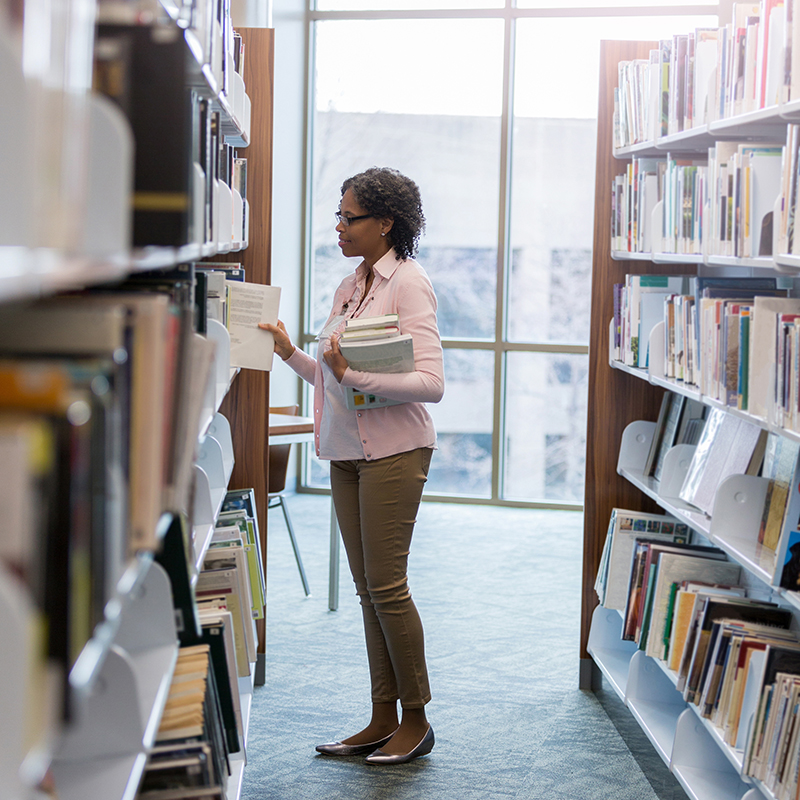 Older woman standing in between book stacks in library