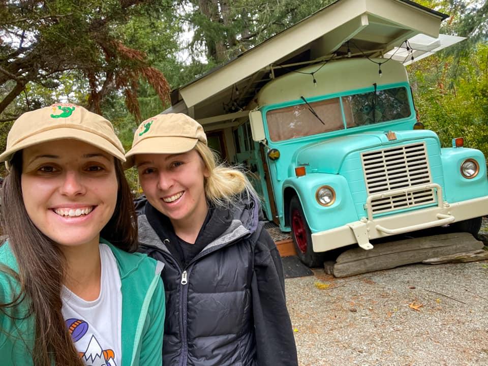 Two women pose in front of blue schoolbus