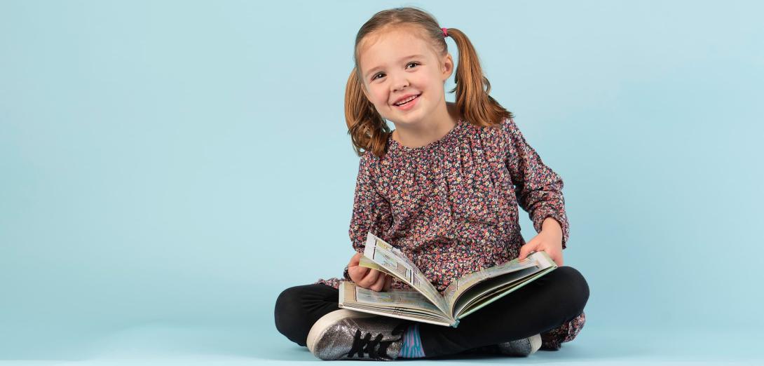 Young girl with pigtails sitting cross-legged with a book 